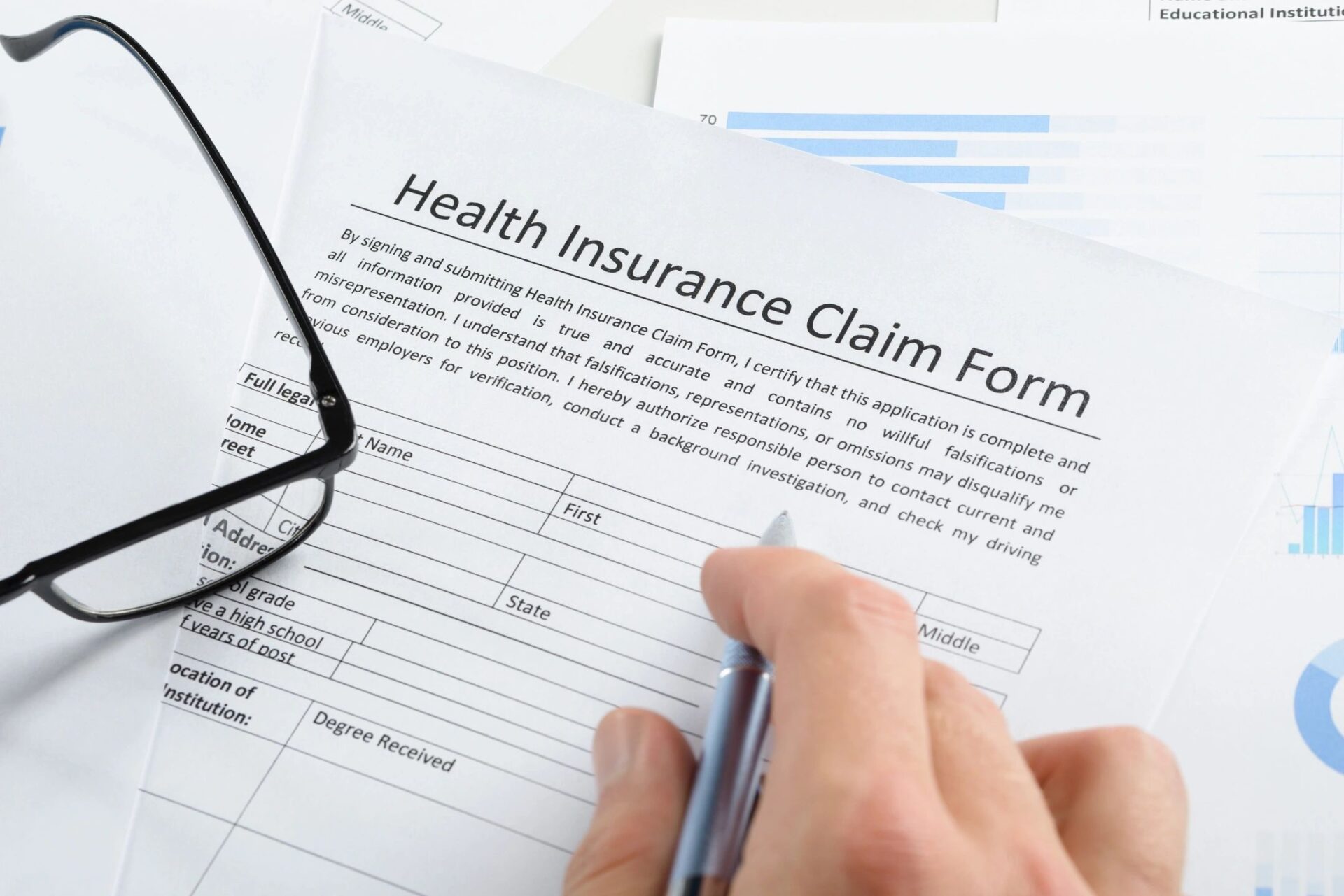 Close-up Of Hand Holding Pen Over Health Insurance Claim Application Form